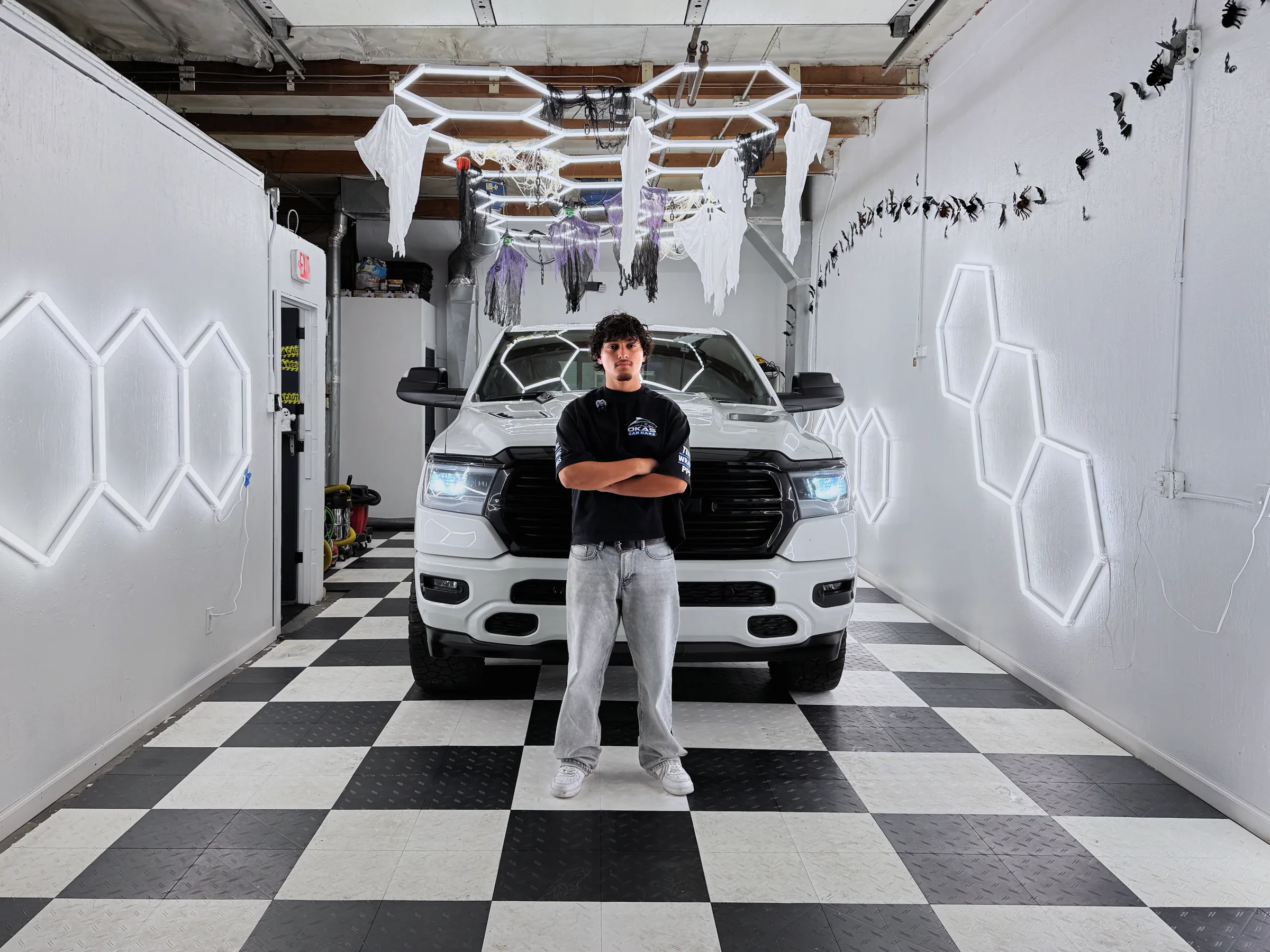 Oka in his bay in Mountain View, arms crossed in front of a white Ram under the hexagon lights